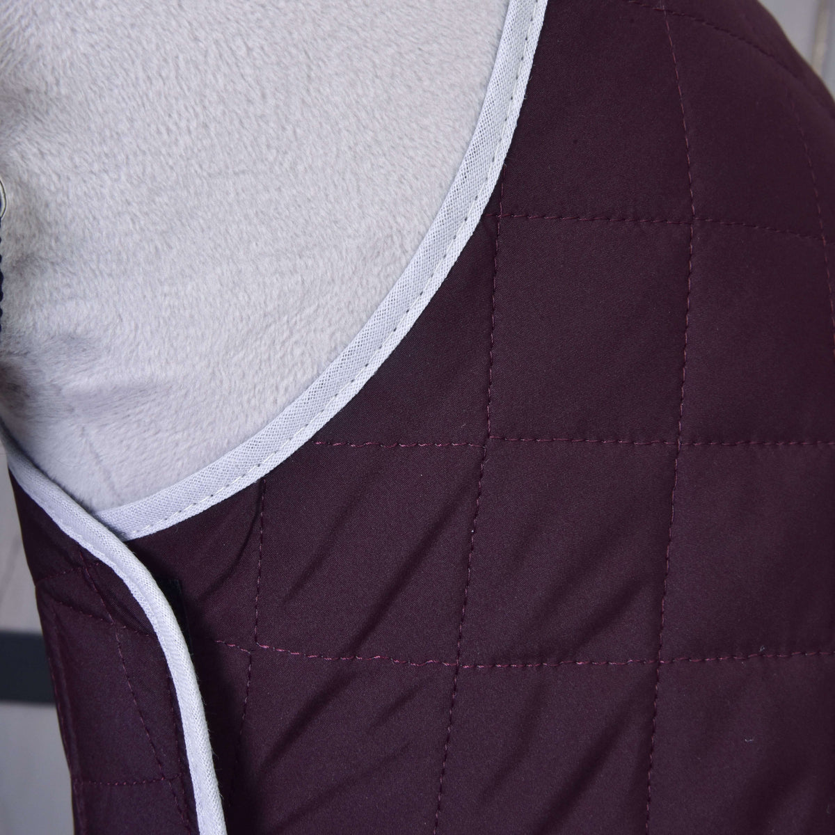 Close-up of Set Purple by Hobby Horse LarDen—a quilted maroon fabric with light grey trim, draped over a soft surface. Ideal as a cozy blanket or for added horse protection.