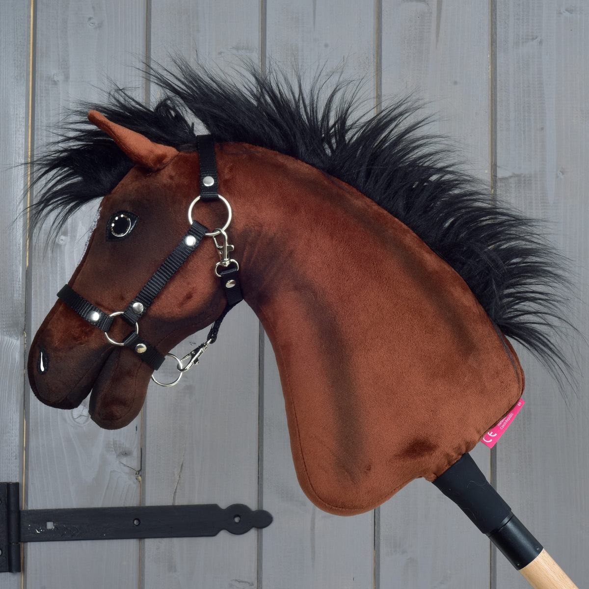 Hobby Horse Roger in left profile, brown plush with a long black mane, a black webbing halter and a light wooden stick