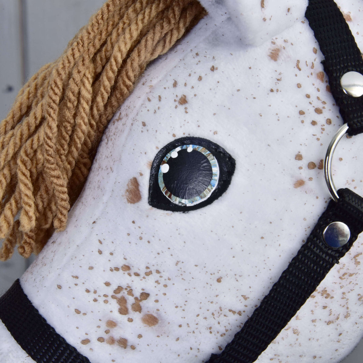 Close-up of Hobby Horse LarDen's "Rufus with Black Halter": a white Appaloosa hobby horse with brown yarn mane, black halter, stitched black and white eye, and plush fabric featuring brown spots like an Appaloosa stallion.