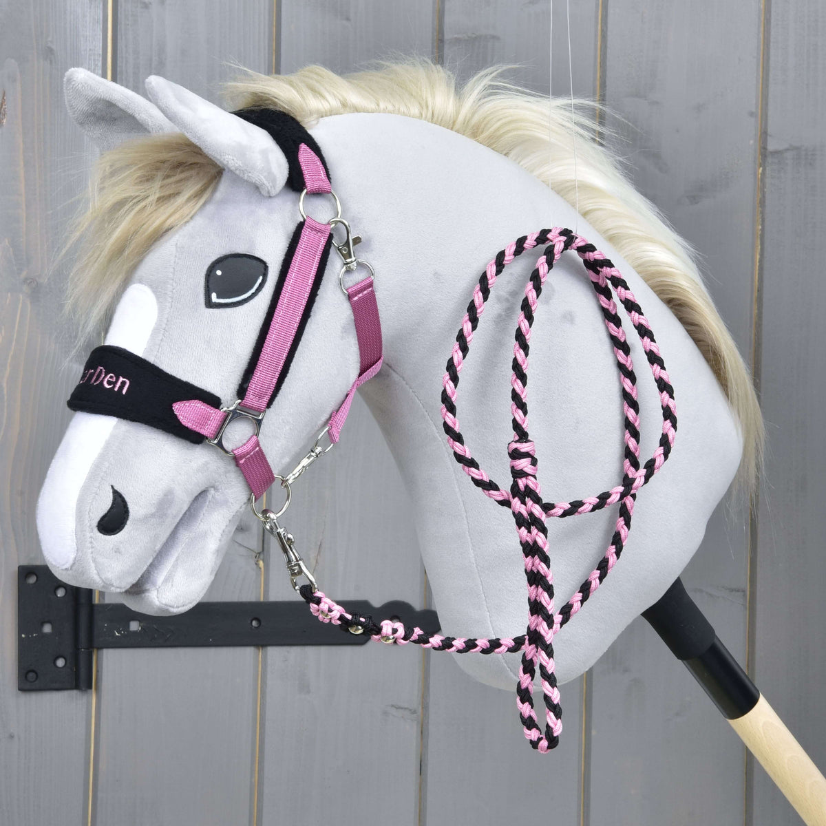 The Hobby Horse LarDen Set LarDen Exclusive Pink features a grey plush hobby horse with a cream mane, pink and black bridle, matching fleece noseband and lead rope on a black stick, shown against a wooden background.