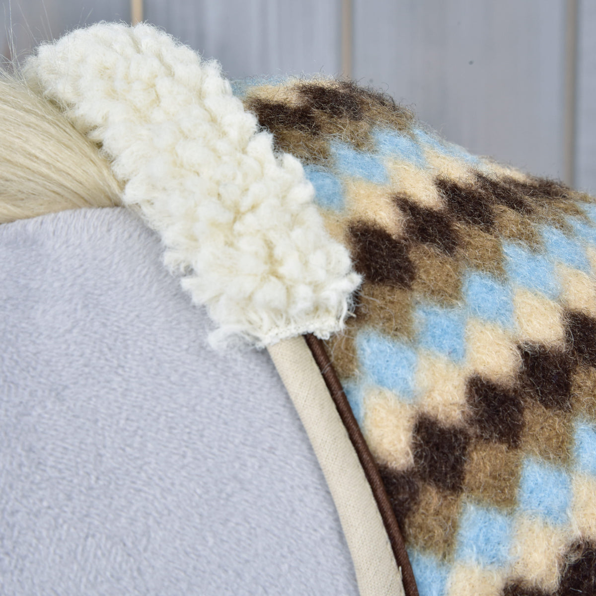 Nærbillede af den cremefarvede krave af krøllet fleece og det beige kantbånd på stalddækkenet Pastel Argyle på en grå kæphest