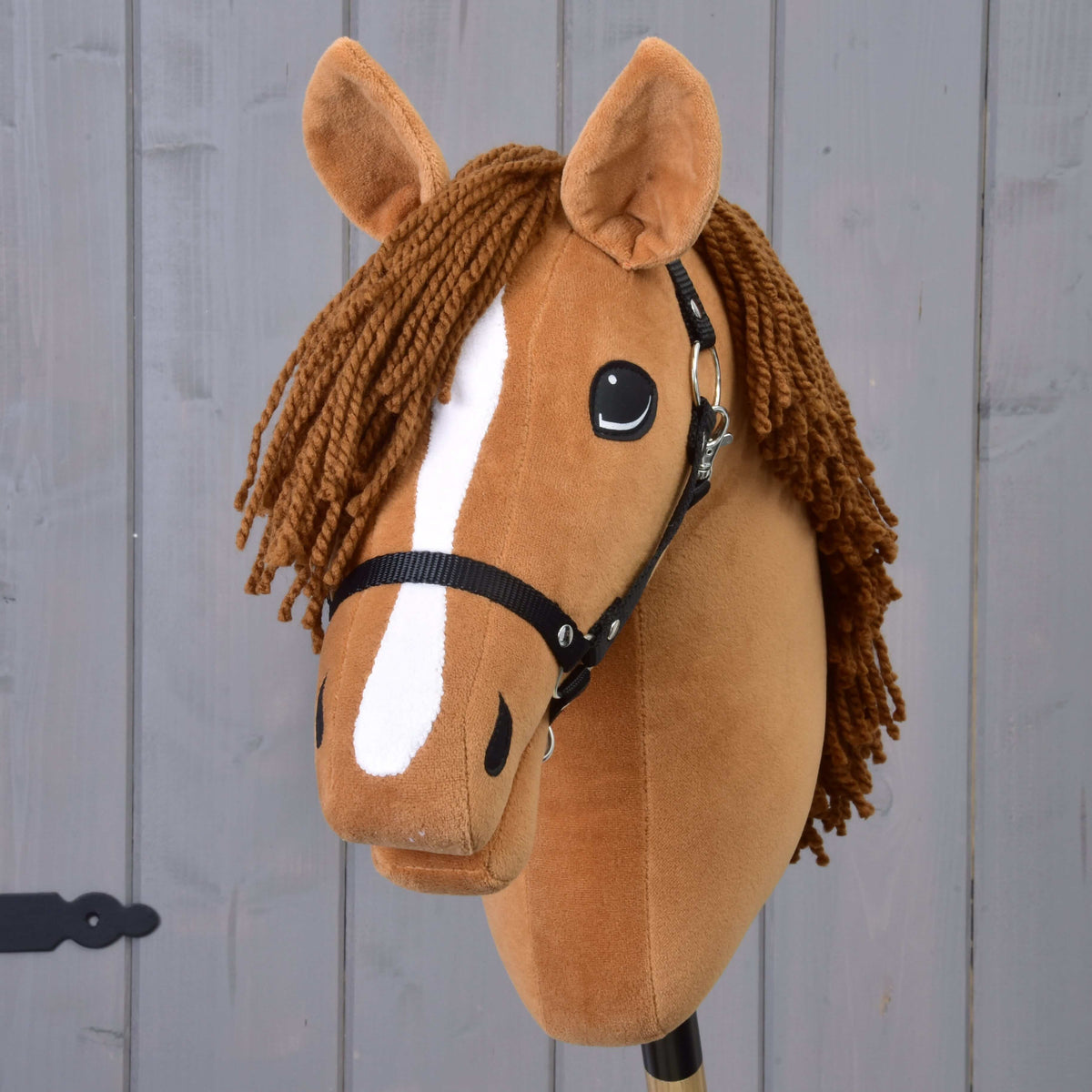 The Hobby Horse Wendy with Black Halter by Hobby Horse LarDen features a brown plush head, braided brown yarn mane, white snout stripe, and black halter, inspired by a chestnut mare and shown on a gray wooden background.