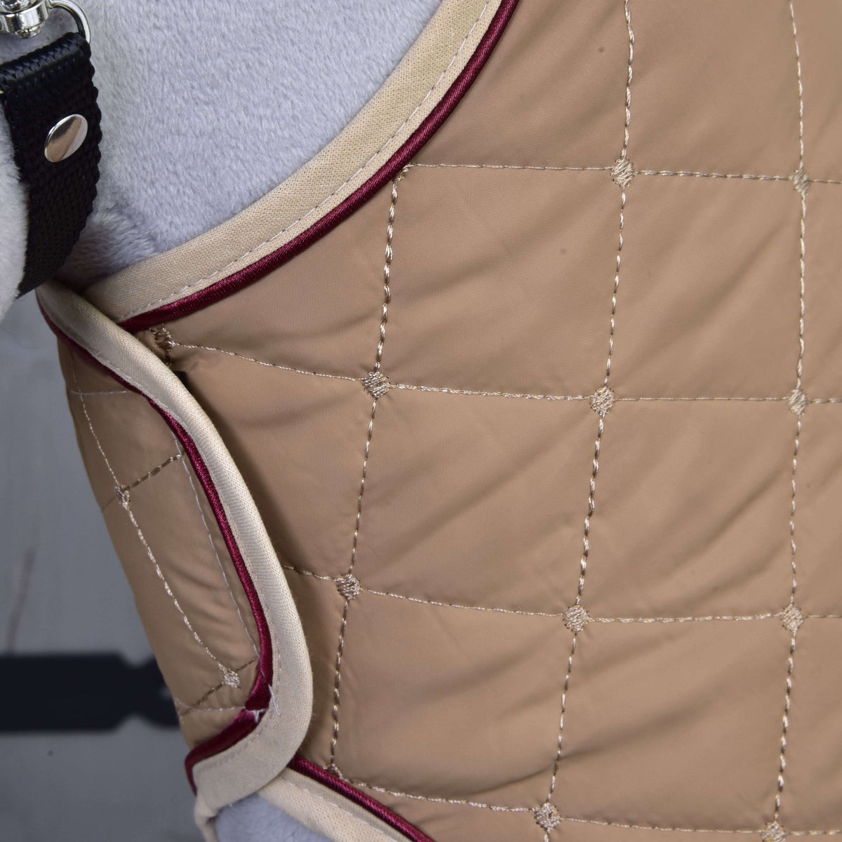 Close-up of the Set Roma by Hobby Horse LarDen: a quilted beige fabric with cream and burgundy trim, stitched square patterns, and a black strap with buckle on the left side.