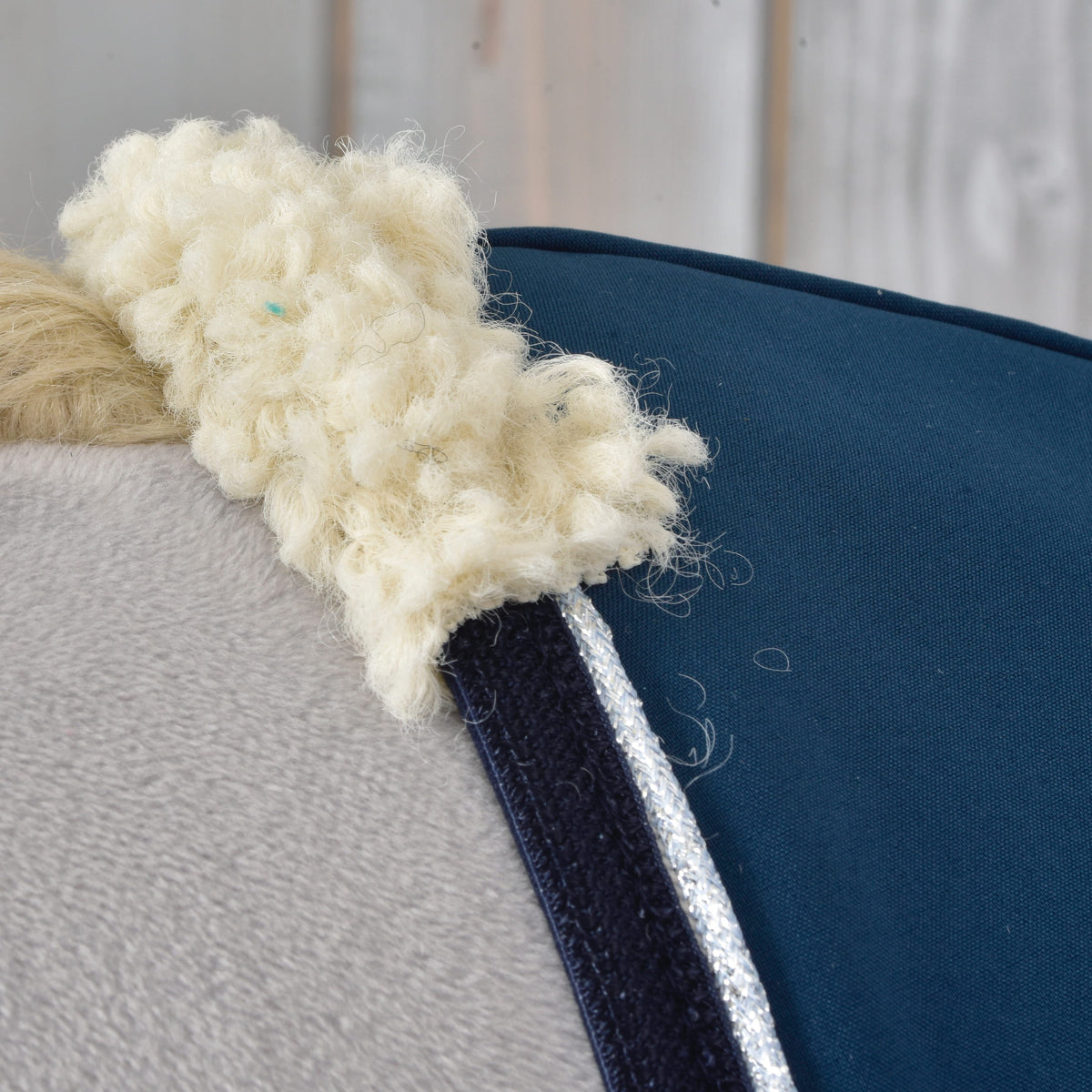 Nærbillede af den cremefarvede krave af krøllet fleece, marineblåt kantbånd og sølvglimmer på stalddækkenet Winter Sky på en kæphest