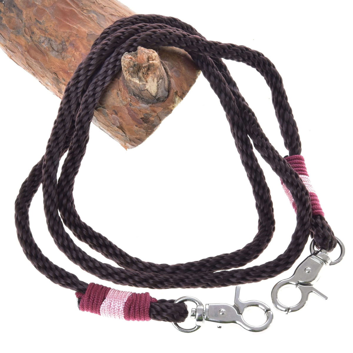 The Reins York by Hobby Horse LarDen are dark brown braided polypropylene reins with metal clips, pink and maroon thread wraps, and are shown coiled on wood—ideal for handmade hobby horse reins.