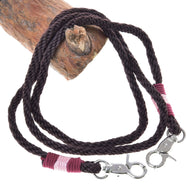 The Reins York by Hobby Horse LarDen are dark brown braided polypropylene reins with metal clips, pink and maroon thread wraps, and are shown coiled on wood—ideal for handmade hobby horse reins.