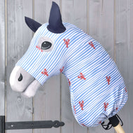 The Hobby Horse LarDen "Hobby Horse protective suit Andromeda (Lycra)" in blue and white stripes with red lobster prints covers the toy horse, which features black eyes, dark blue ears, and a light grey snout against a wooden wall.