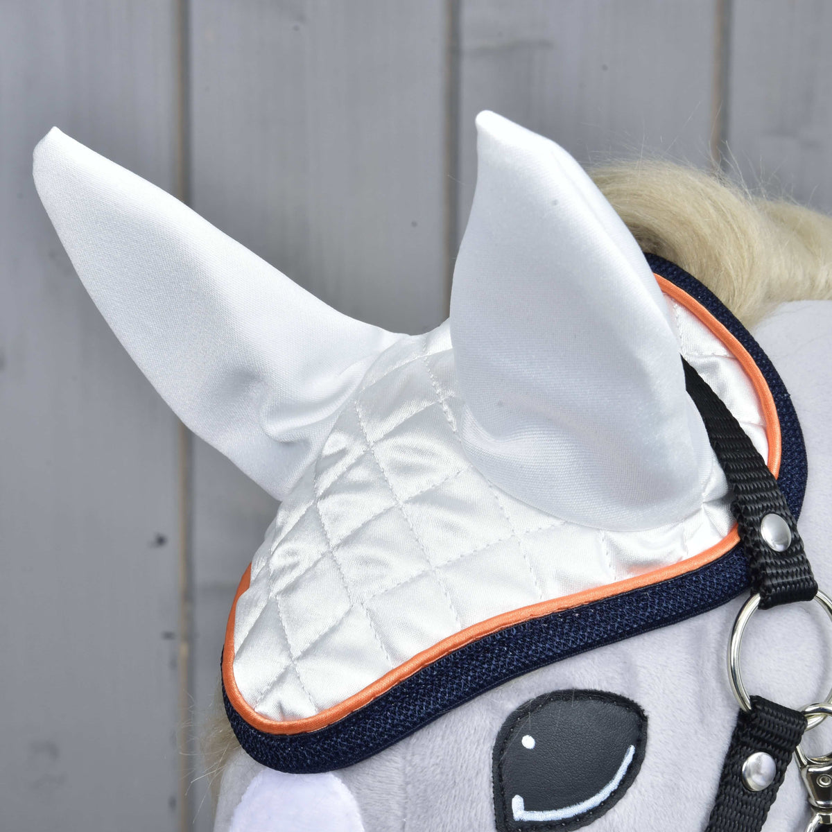 Close-up of the white quilted satin ear bonnet with orange piping and navy binding over the stitched eye