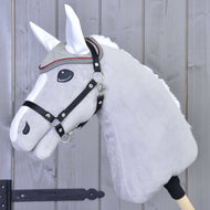 A close-up of a gray plush hobby horse by Hobby Horse LarDen, shown with a bridle, decorative brow band, and the Ear Bonnet Silver Eleganza for insect protection, set against a wooden fence.