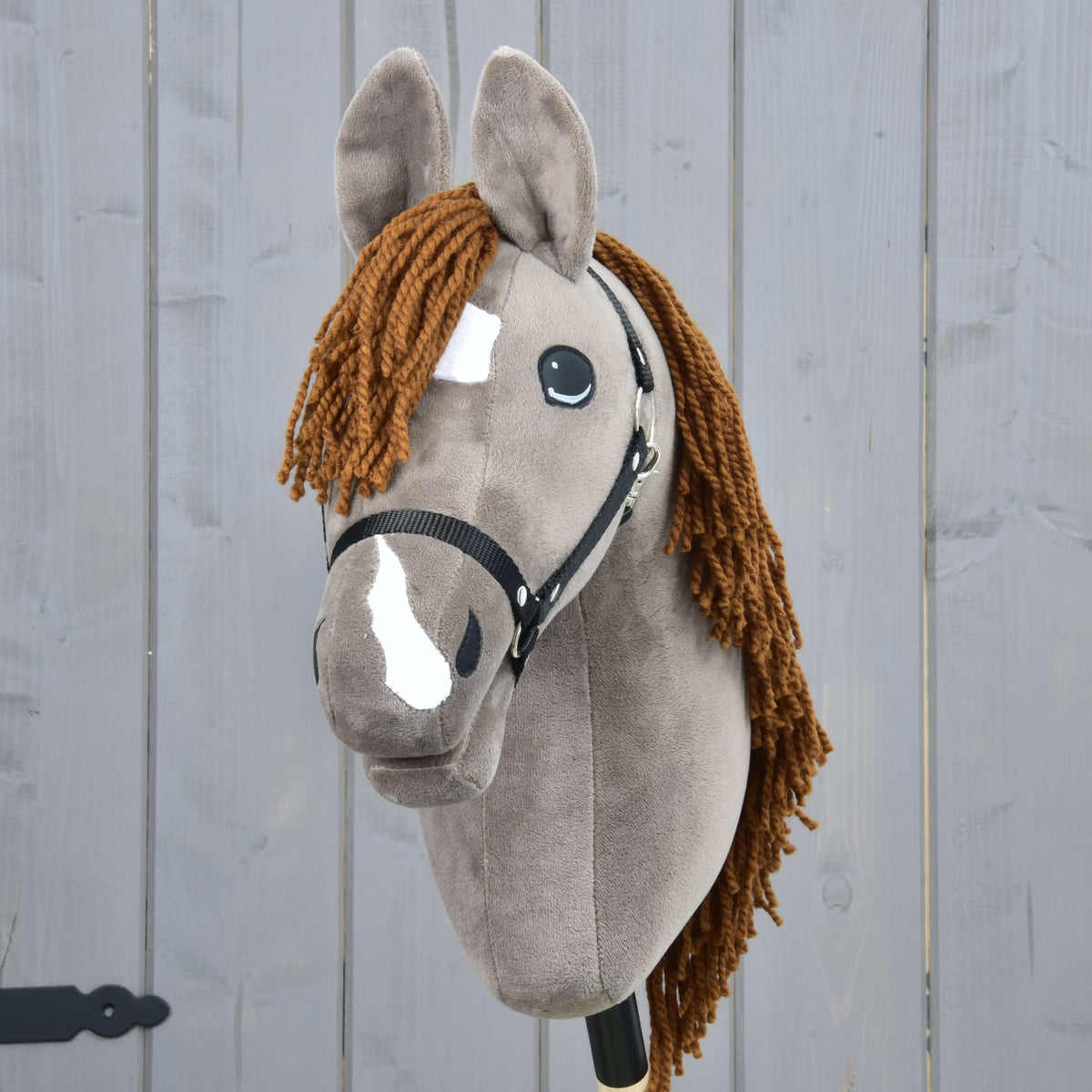 The Hobby Horse LarDen Hobby Horse Chanell with Black Halter features a gray coat, brown yarn mane, white face patches, large expressive eyes, and is displayed against a gray wooden background.