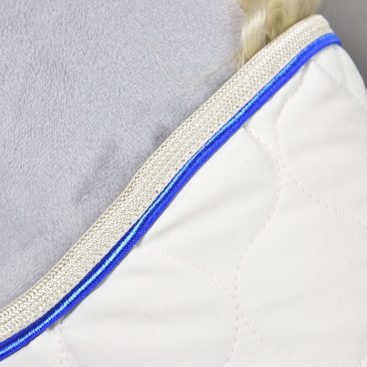 Detalje af halsåbningen på dækkenet Cream Pearl: kongeblå paspoil og skinnende beige flettet kant på cremefarvet quiltning