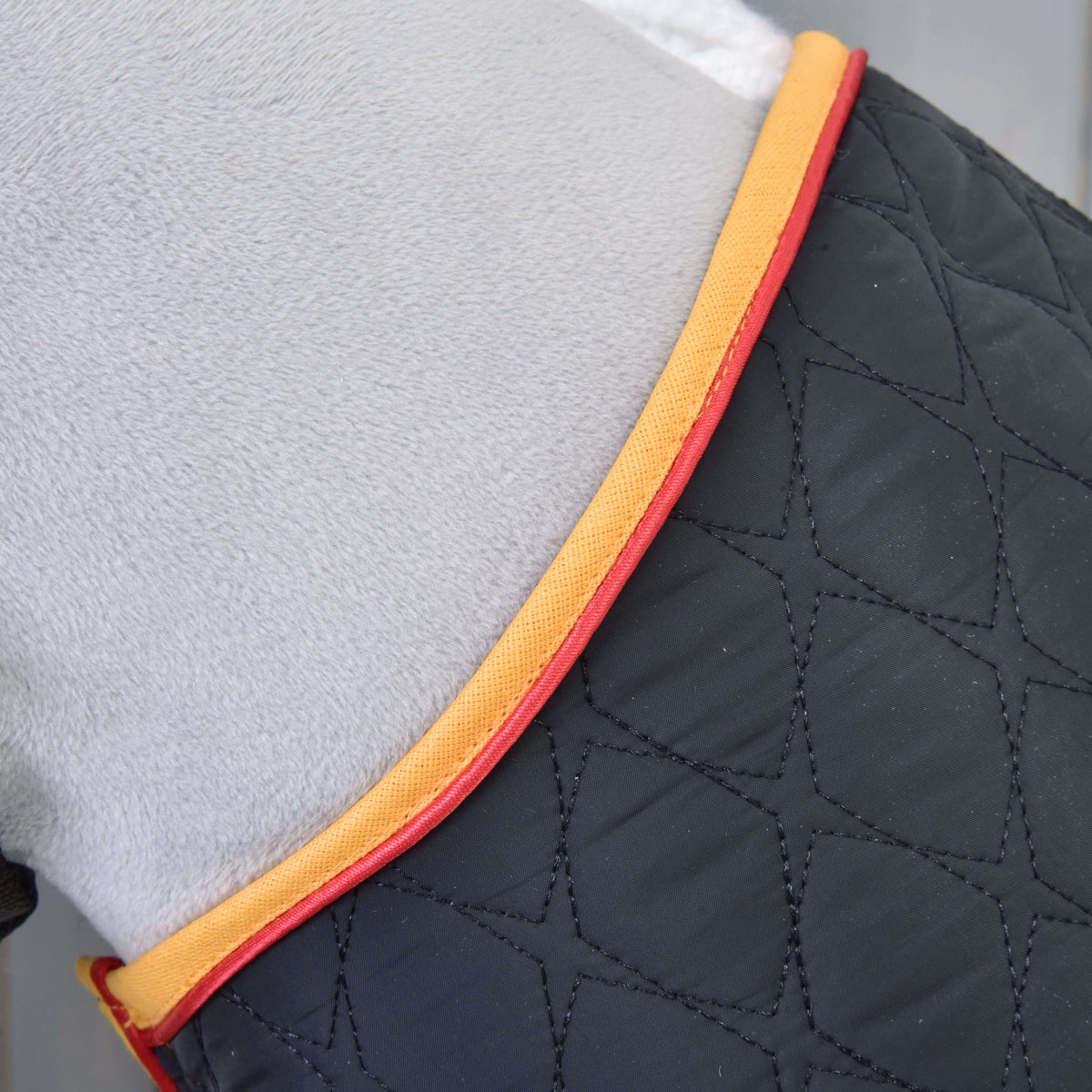 Close-up of a quilted black Blanket Flag by Hobby Horse LarDen, featuring a diamond pattern with yellow and red trim, beside a light grey surface—crafted for comfort and style.