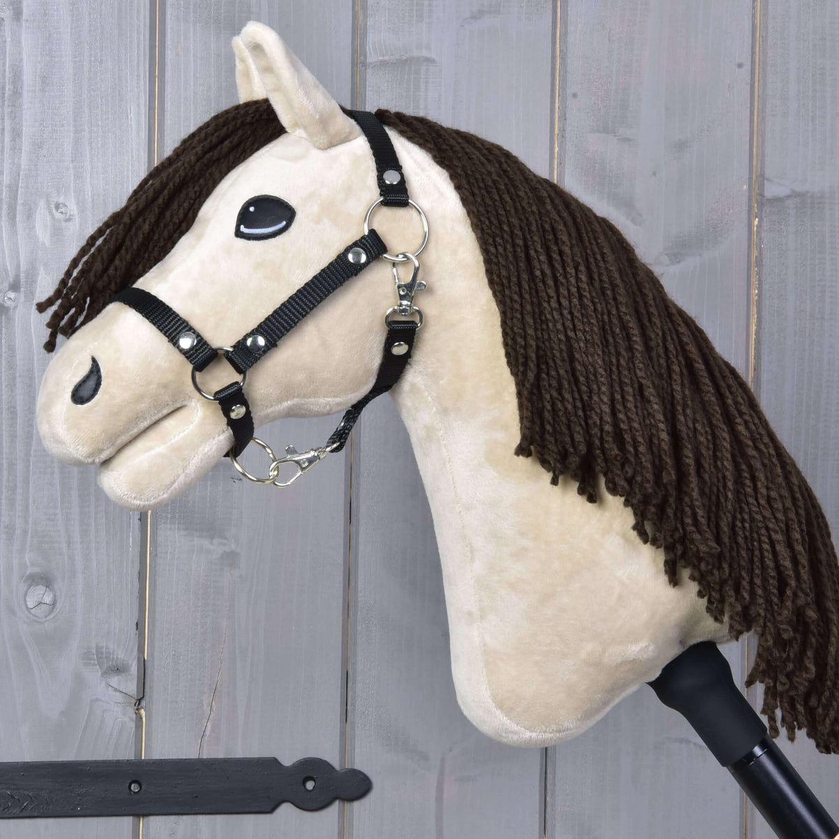 The Hobby Horse LarDen Hobby Horse Frederik LD features a plush Mustang head with brown yarn mane, black halter, and reins on a stick, shown against a wooden plank background.