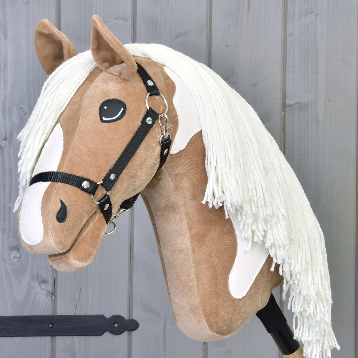 Hobby Horse LarDen’s Hobby Horse Fury with Black Halter features a tan and white face, large black eyes, white yarn mane, and is shown mounted on a stick against a gray wooden background.