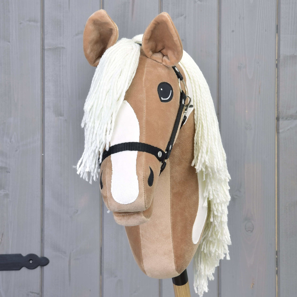 The Hobby Horse Fury with Black Halter by Hobby Horse LarDen features a tan and white face, black halter, and long white mane—resembling an American Paint Horse—set against a gray wooden background. Perfect for imaginative adventures.