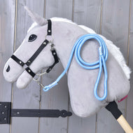 The Hobby Horse LarDen "Hobby Horse - rope stripe Heaven" is a gray plush hobby horse with a white mane, black bridle, blue-and-white leash, and stick base, displayed against a light wooden wall—perfect for leading or lunging play.