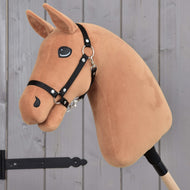 The Hobby Horse LarDen "Build your horse" features a customizable brown fabric head, black bridle, and cartoon eyes on a wooden stick, shown in front of a gray wood-paneled door.