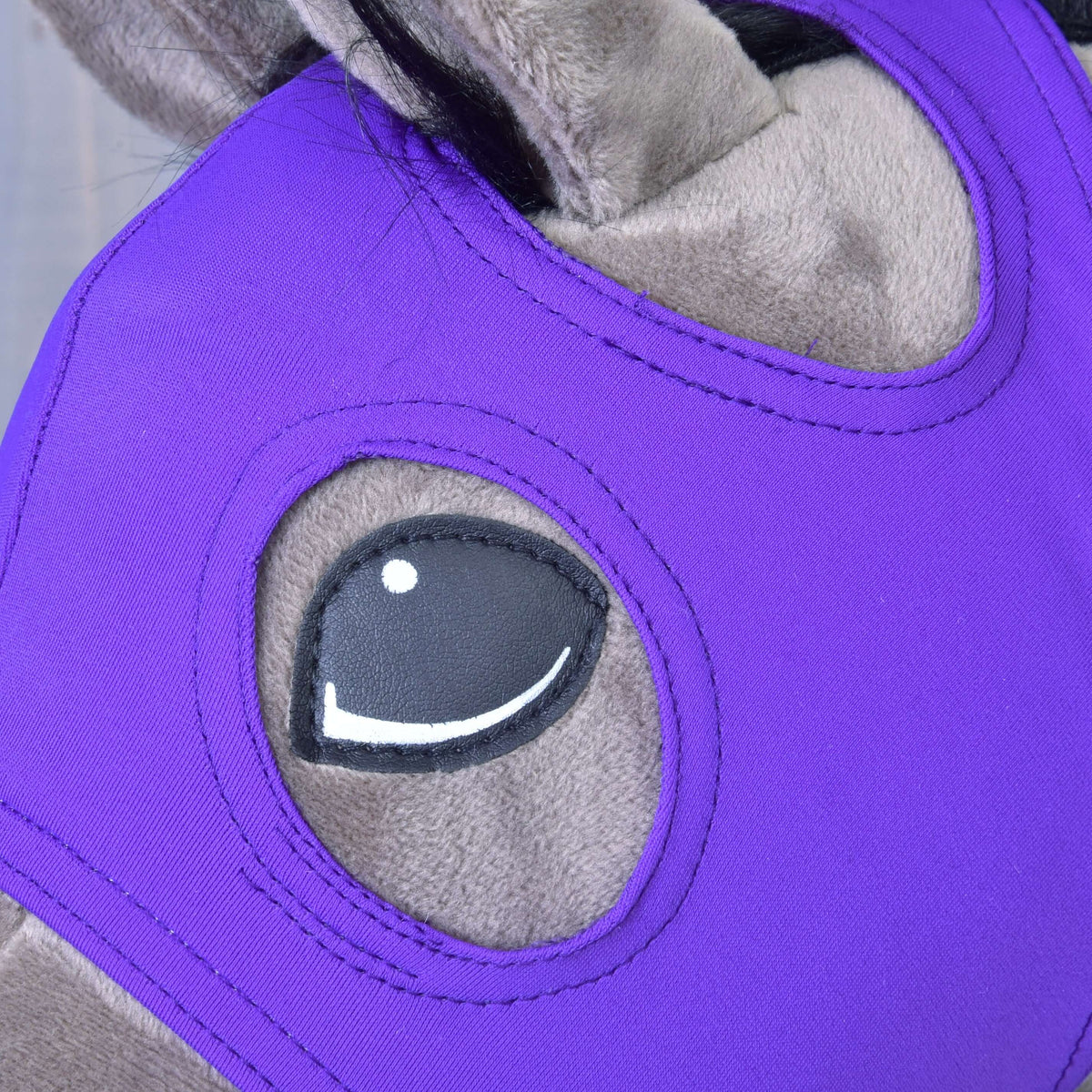 Close-up of a gray horse wearing the Hobby Horse LarDen "Horse Mask without ears Indigo," a bright purple, washable PES mask with a cartoon-like eye design and an opening for the eye.