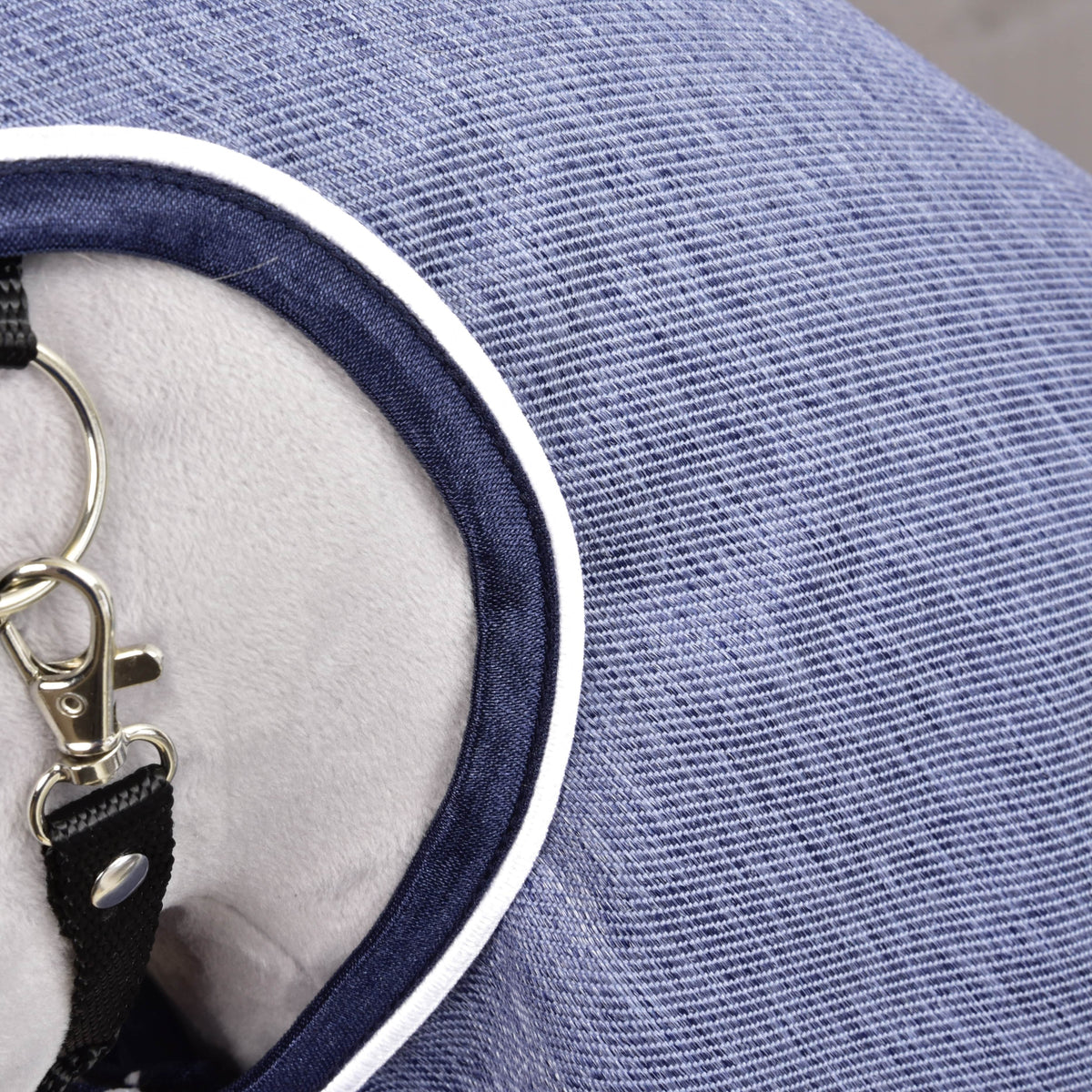 Nærbillede af regndækkenet Jeans: blåt stof med denimstruktur, mørkeblå kant og hvid paspoil ved halsåbningen