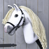 The Hobby Horse LarDen Little Lady with a black halter features a white body and long cream-colored yarn mane, standing against wooden panels and reflecting the elegance of Pura Raza Española dressage.