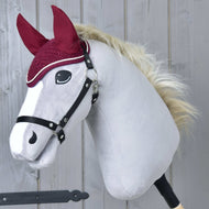 The Hobby Horse LarDen Ear Bonnet Crocheted Lux Maroon is shown on a plush stick horse toy with a white face, black bridle, fluffy blond mane, maroon fabric ears, and matching bonnet against a gray wooden background.