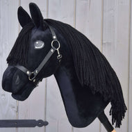 The Hobby Horse LarDen "Mahal with Black Halter" is a plush Friesian-style hobby horse with a black mane, black halter, and white eye detail, mounted on a wooden stick and shown against a light gray wooden wall.