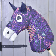 The Hobby Horse LarDen "Hobby Horse protective suit Mandala (Lycra)" features a fabric head with purple, pink, and orange geometric patterns, black ears, and a white muzzle, displayed with a stylish accessory against a gray wooden background.