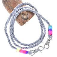 The Reins Manhattan by Hobby Horse LarDen is a gray and white braided polypropylene rope with metal clasps and colorful yellow, blue, pink, and purple thread wraps, coiled around a piece of wood.