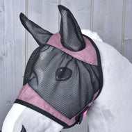 A white horse wears the Hobby Horse LarDen Fly Mask De Luxe Pink, a washable black and pink mesh mask covering its ears and face, standing before a light gray wooden background.