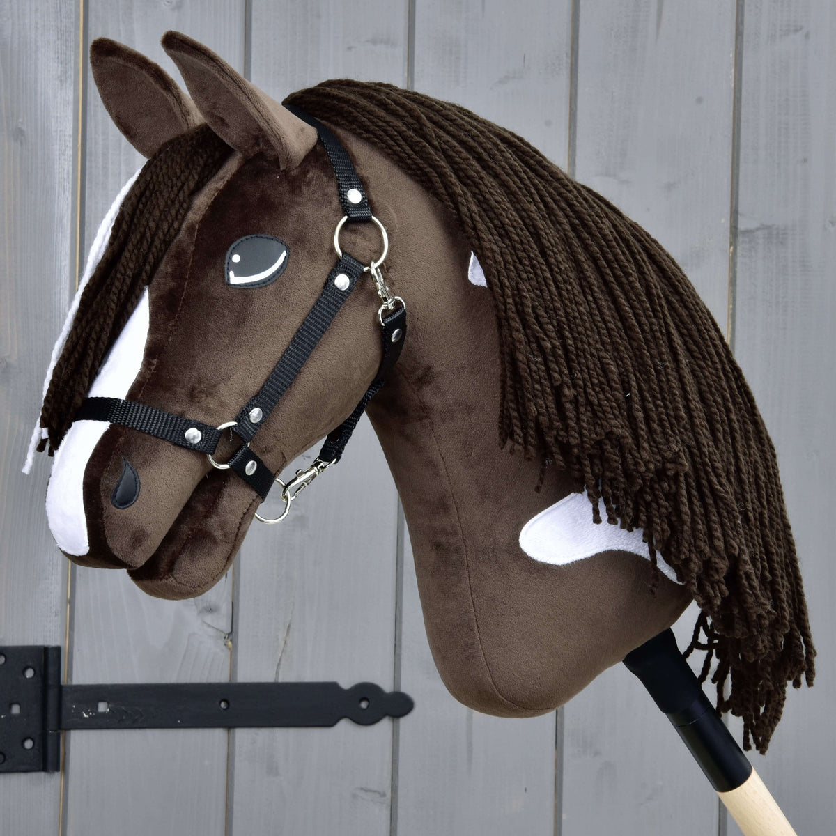 The Hobby Horse Monte with Black Halter by Hobby Horse LarDen features a brown and white design inspired by the American Paint Horse, black halter, white patches, long dark yarn mane, and is mounted on a wooden stick.