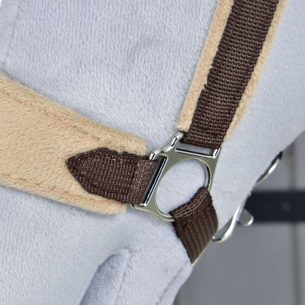 Close-up of the silver side ring joining the dark brown cheek strap to the beige fleece noseband of the brown fur halter