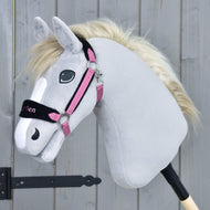 A plush grey Hobby Horse LarDen with a white mane features a Fur Halter LarDen Pink and sits on a stick in front of a wooden fence.