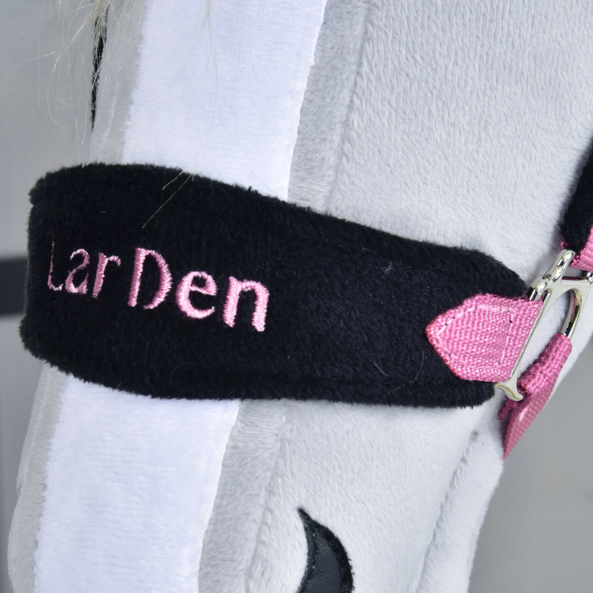 Close-up of the Hobby Horse LarDen Fur Halter Pink, with pink embroidery on a black strap and metal-and-pink buckle, resting on light gray plush—a stylish choice for your hobby horse.