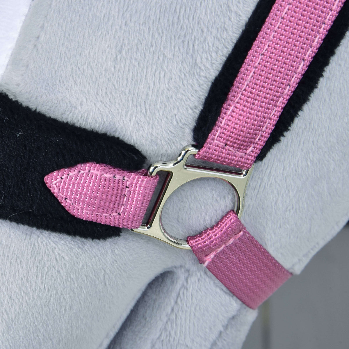 Close-up of the Fur Halter LarDen Pink from Hobby Horse LarDen, showing its pink fabric strap with a shiny silver buckle on a soft, light gray surface and accented by black trim.