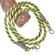 The Hobby Horse LarDen "Hobby Horse - Reins lemon stripe" is a yellow, black, and gray striped rope leash with metal clips on both ends, coiled on wood against a white background—ideal as handmade or hobby horse reins.