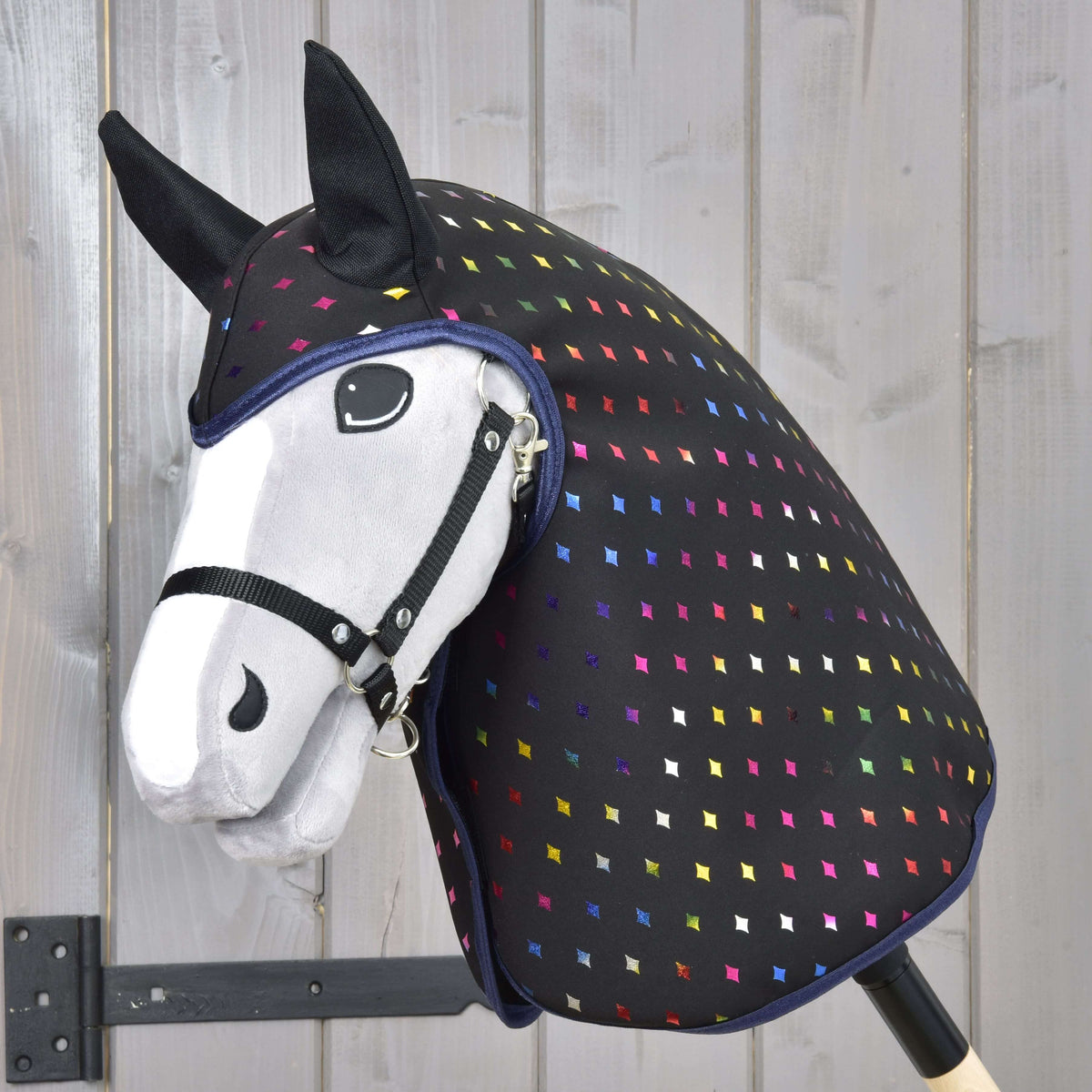Light grey Hobby Horse in a black halter wearing the Raincoat Sparkling Queen, black with rainbow diamonds and black ears