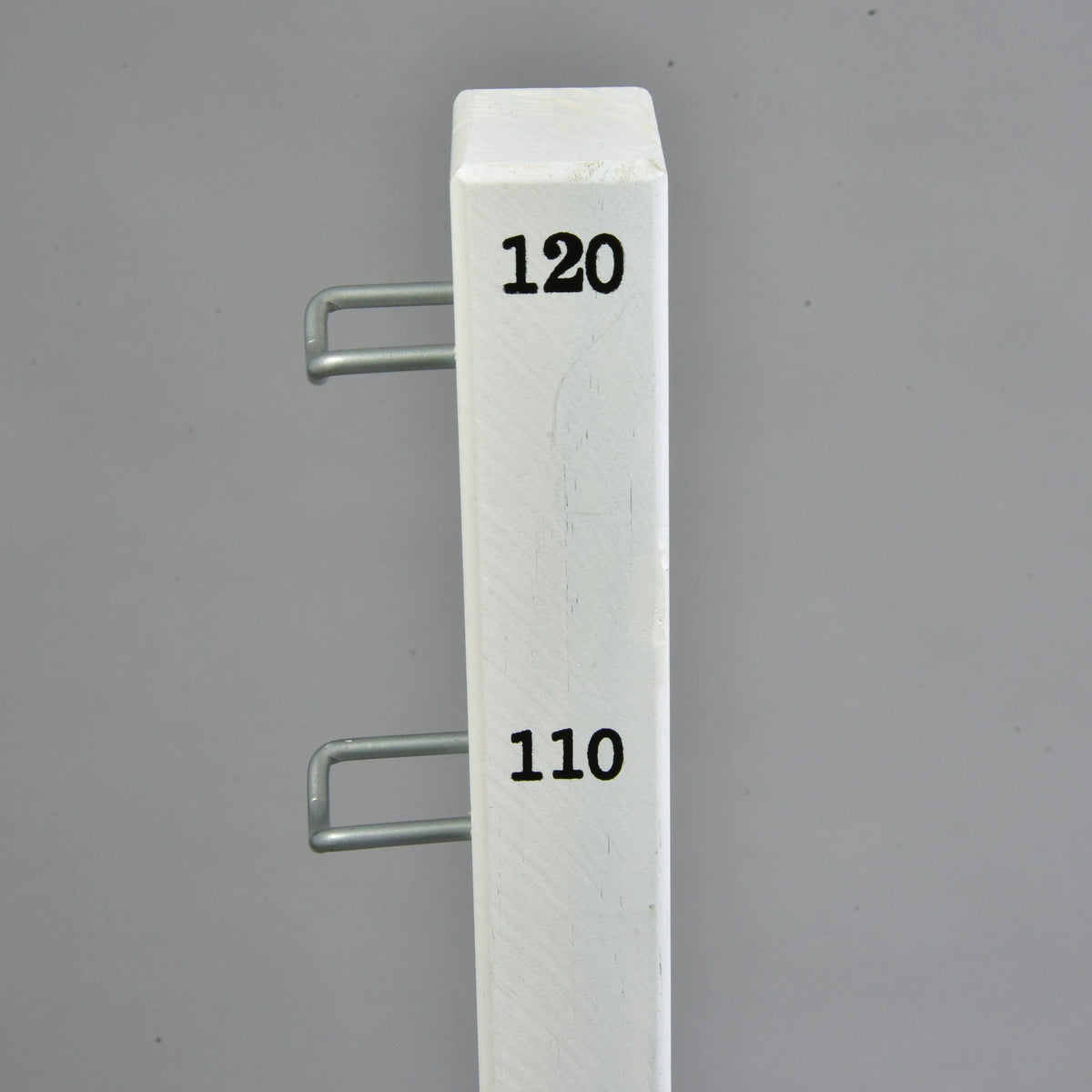 Top of a white jump stand with black 110 and 120 height marks and two U-shaped metal hooks