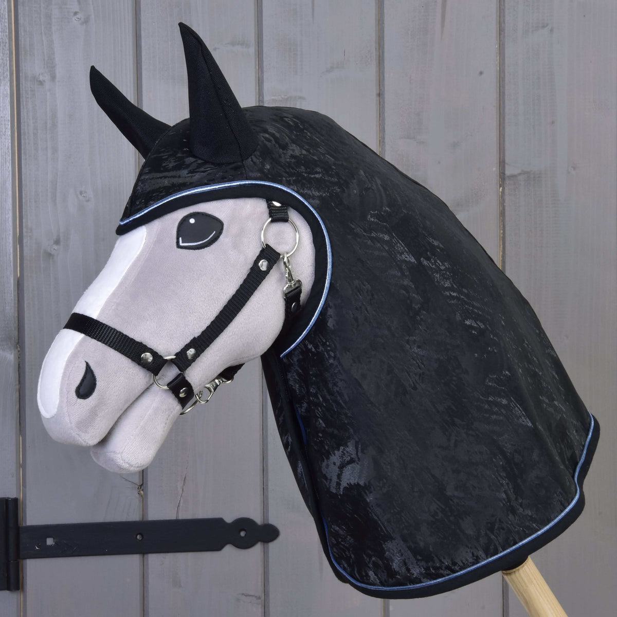 Grey Hobby Horse in a black halter wearing the black marbled raincoat with black ear covers and light blue piping
