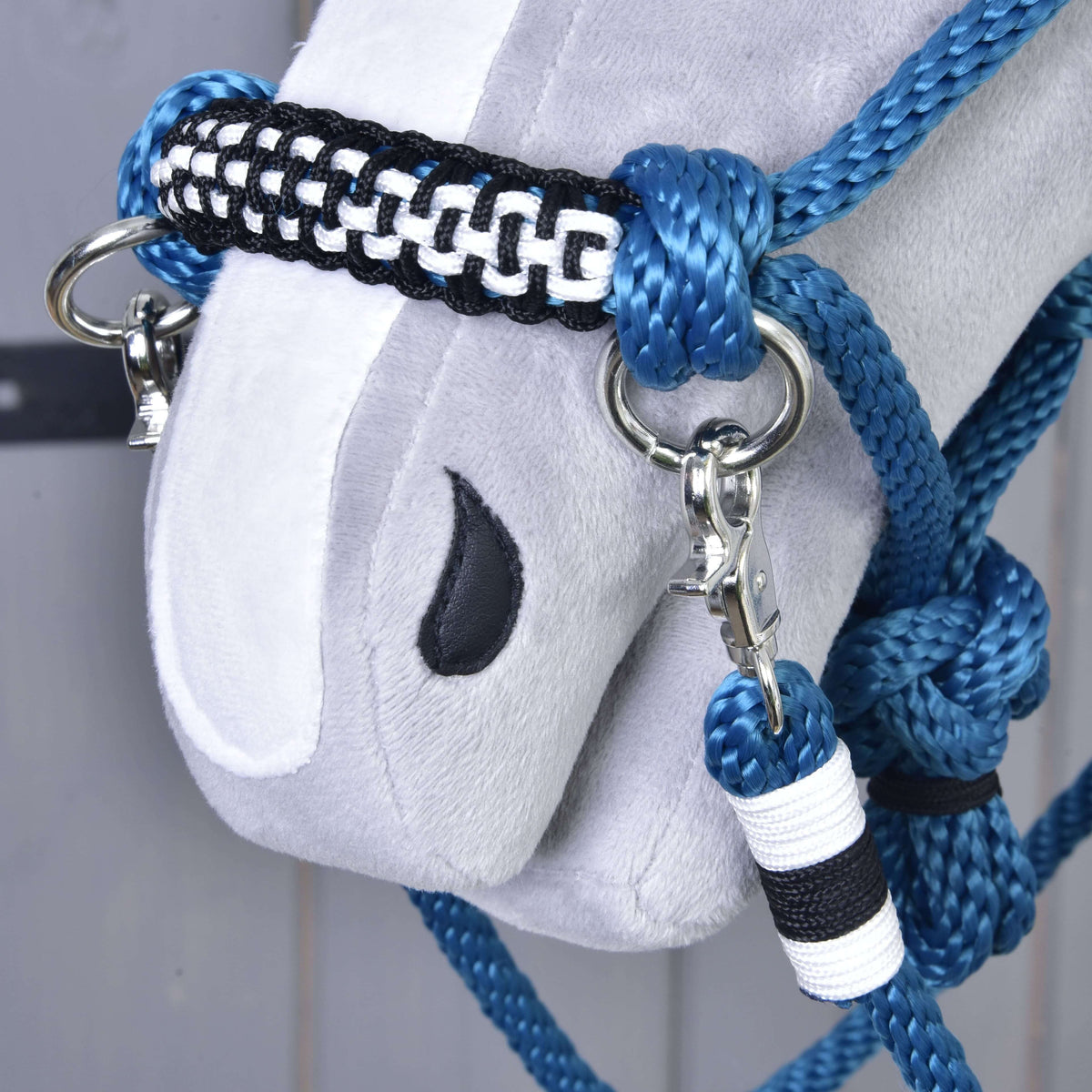 Close-up of a soft gray horse head with an embroidered black eye, wearing the Hobby Horse LarDen Rope set Chess—a handmade blue, black, and white halter with metal rings and clips.