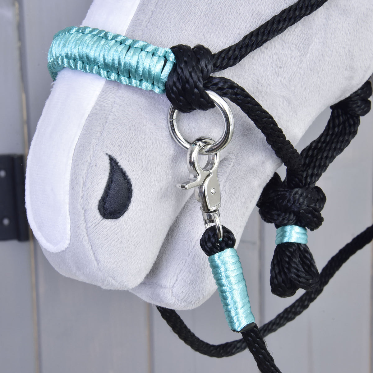 Close-up of a gray Hobby Horse head wearing the Hobby Horse LarDen Rope set Turquoise halter and matching reins with metal ring and clasp, set against a light gray wooden background.