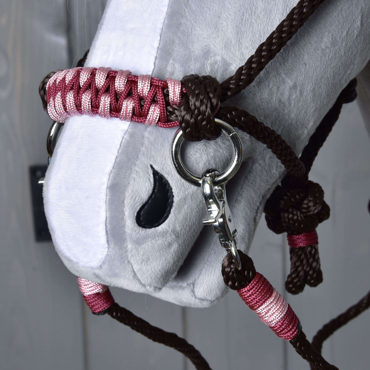 A close-up of a white plush Hobby Horse LarDen head, featuring the Rope set York—a brown and pink braided halter with metal rings—and black stitched nostril detail.