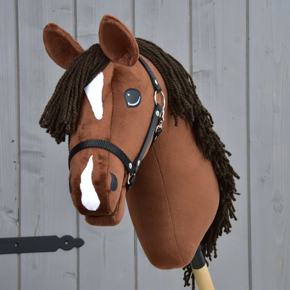 The Hobby Horse LarDen Rocky with Black Halter features a brown Thoroughbred-style head, white facial markings, and a dark yarn mane, shown against a gray wooden background.