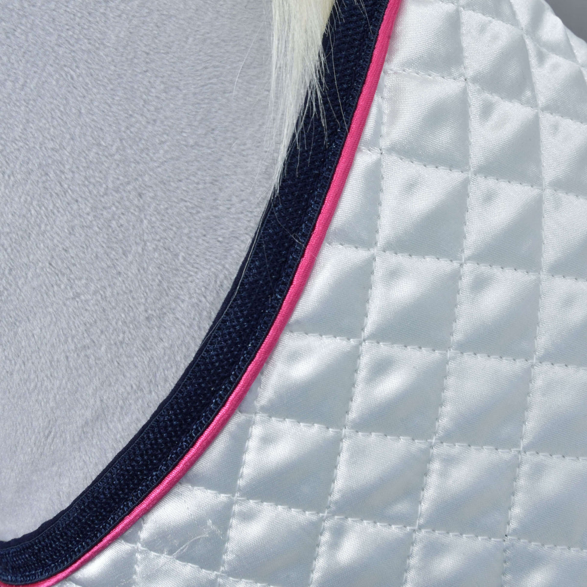 Close-up of the Set Beautiful Star by Hobby Horse LarDen: a quilted white fabric with navy and pink trim, draped over a light gray fuzzy surface. A small section of white hair appears at the top.