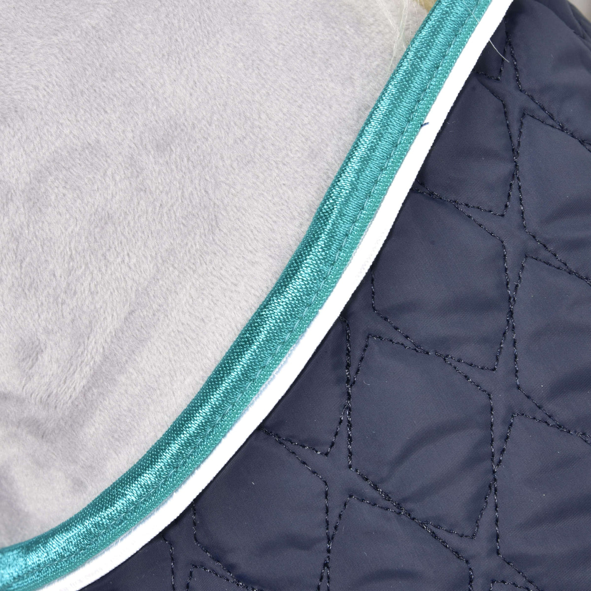 Close-up of the Set Supreme Turquoise blanket by Hobby Horse LarDen, featuring quilted dark blue fabric with geometric stitching, teal trim, and white piping—ideal for protecting your horse.