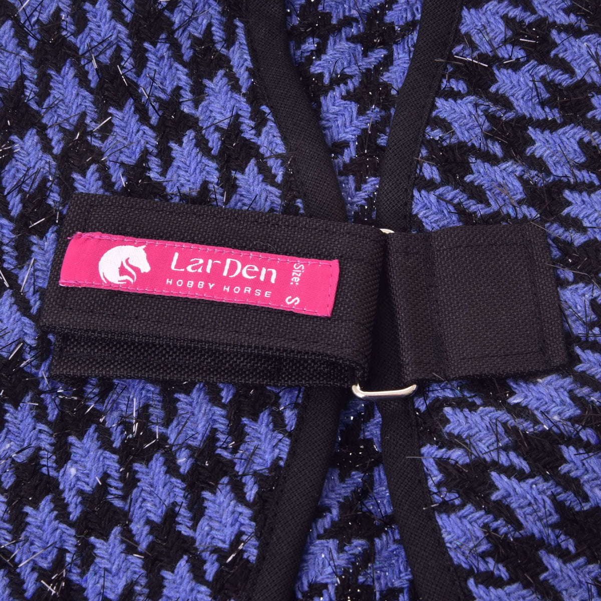Close-up of the Stable Blanket Blue by Hobby Horse LarDen, featuring a blue and black houndstooth pattern, black strap, and a pink LarDen Hobby Horse S label attached to the strap.