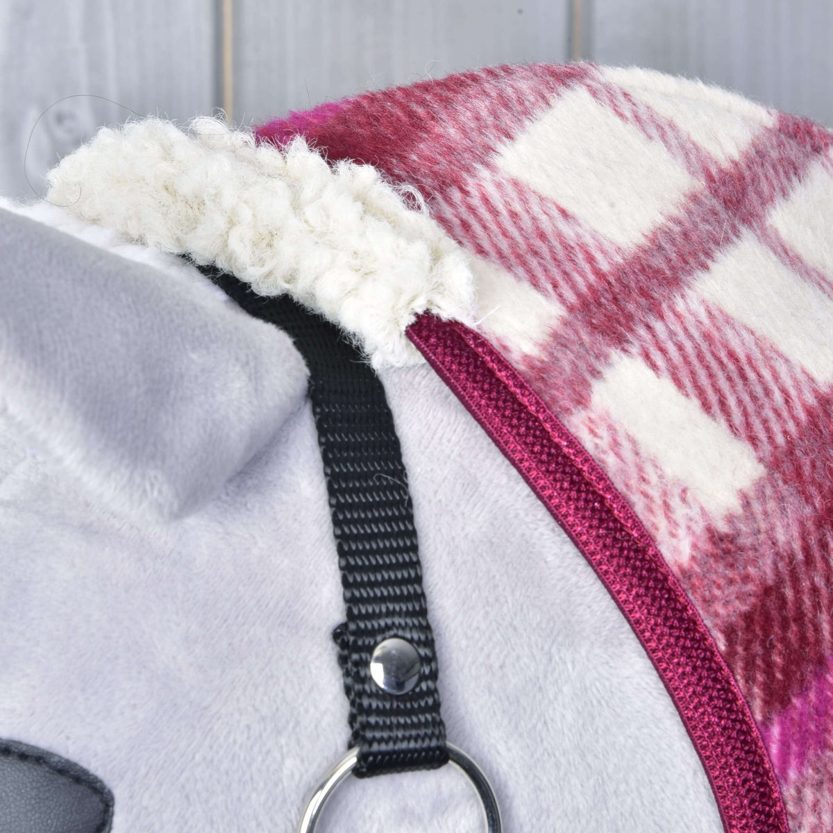 Close-up of a gray and white stuffed animal wearing the Stable Blanket LarDen by Hobby Horse LarDen—a red and white plaid fleece blanket with a black strap and metal ring; plush material features visible stitching and soft textures.
