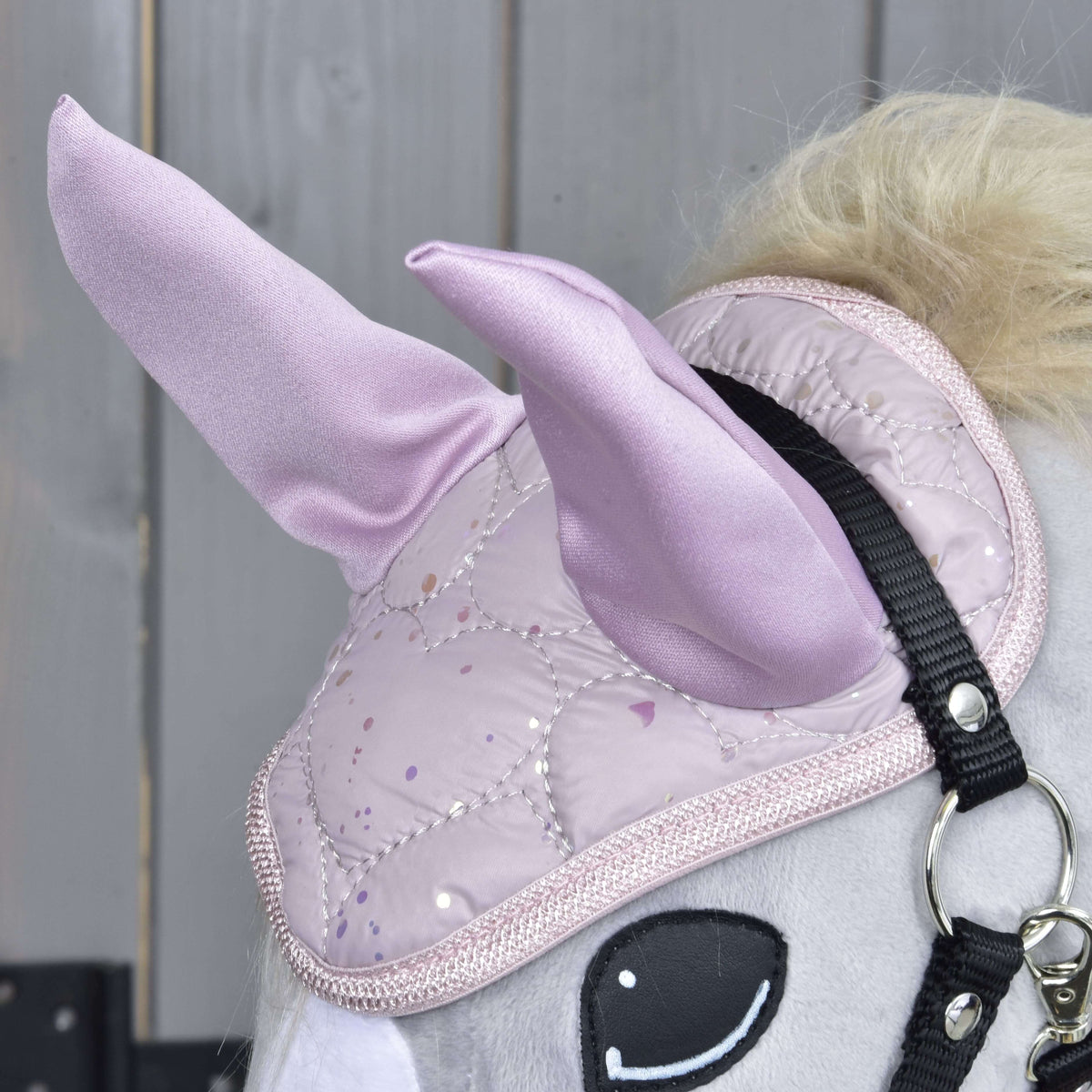 A close-up of the Hobby Horse LarDen Set Sweetest Heart shows its light gray head with a shiny quilted pink unicorn horn, ear bonnet, black bridle, and a wooden background.