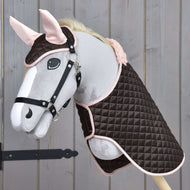 The Hobby Horse LarDen Set Thermo Sweety features a plush hobby horse with a bridle, dressed in a quilted brown and pink blanket and matching ear bonnet set, displayed against a wooden background.