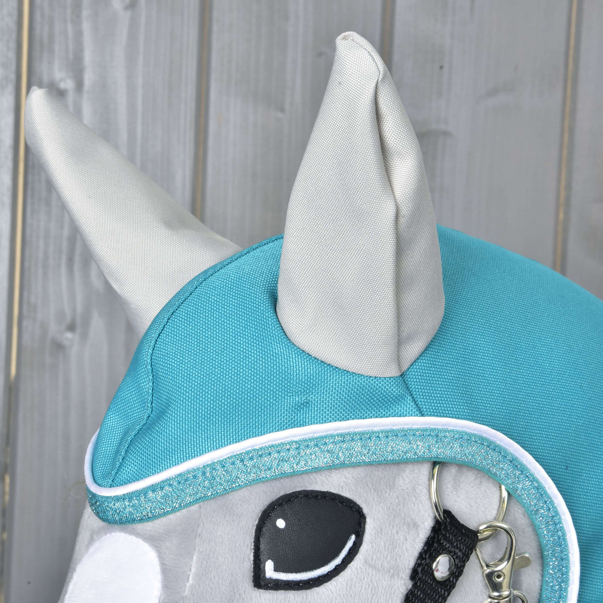 Close-up of the Raincoat Turquoise hood on a grey Hobby Horse: light grey ears and glittery trim with white piping