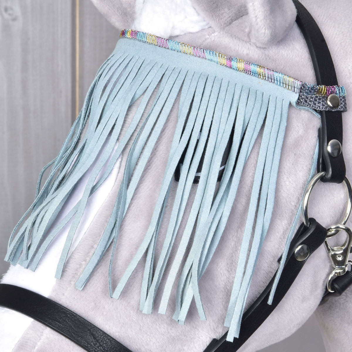 Close-up of the pale turquoise fringe and pastel rainbow band next to the silver snap hook on a grey Hobby Horse
